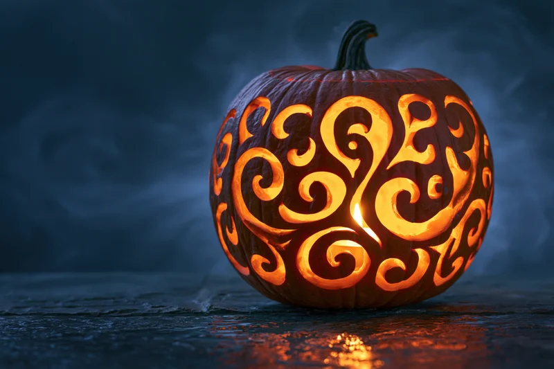 Carved pumpkin with swirling filigree design glowing in the dark on a wet stone surface