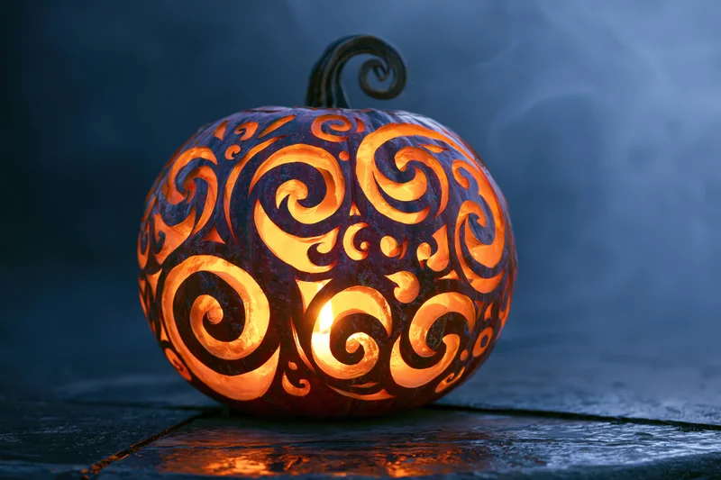 Carved pumpkin with swirling filigree design glowing in the dark on a stone surface