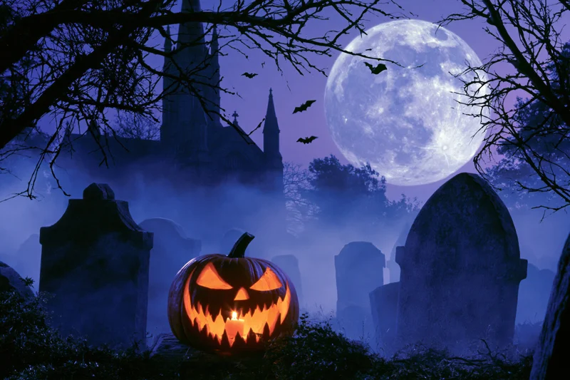 Glowing jack-o-lantern in foggy graveyard at night with full moon and church in background