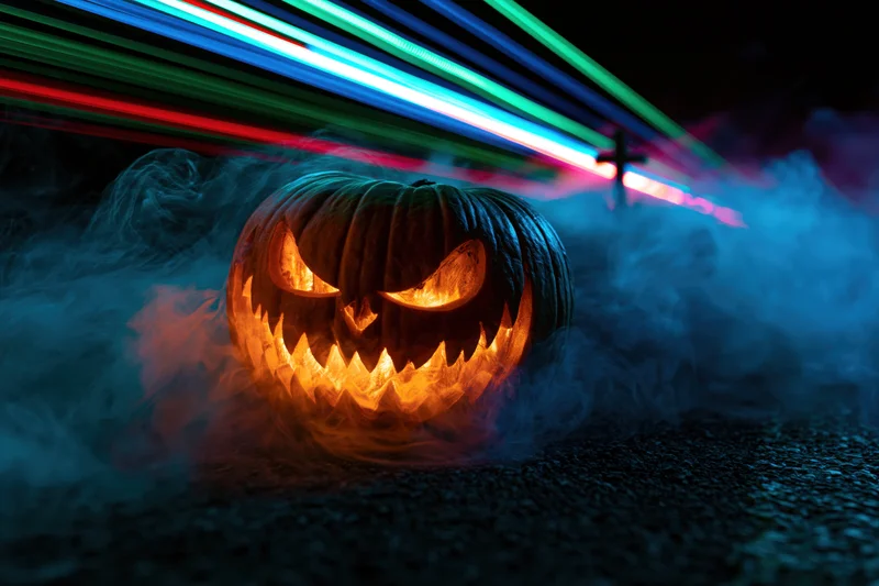 Carved jack-o-lantern with glowing evil grin surrounded by smoke and neon light streaks at night