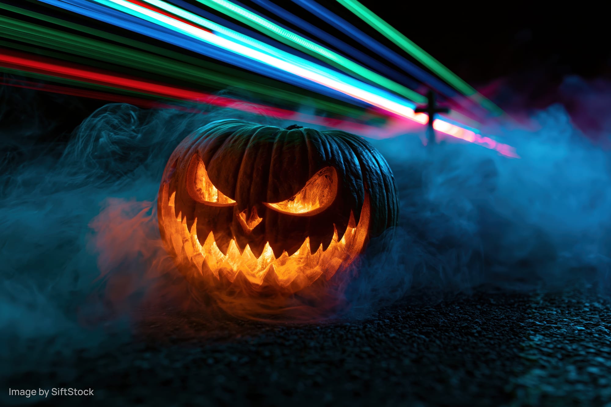 Carved jack-o-lantern with glowing evil grin surrounded by smoke and neon light streaks at night