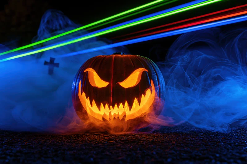 Carved jack-o-lantern with glowing evil grin surrounded by blue smoke and neon light trails at night