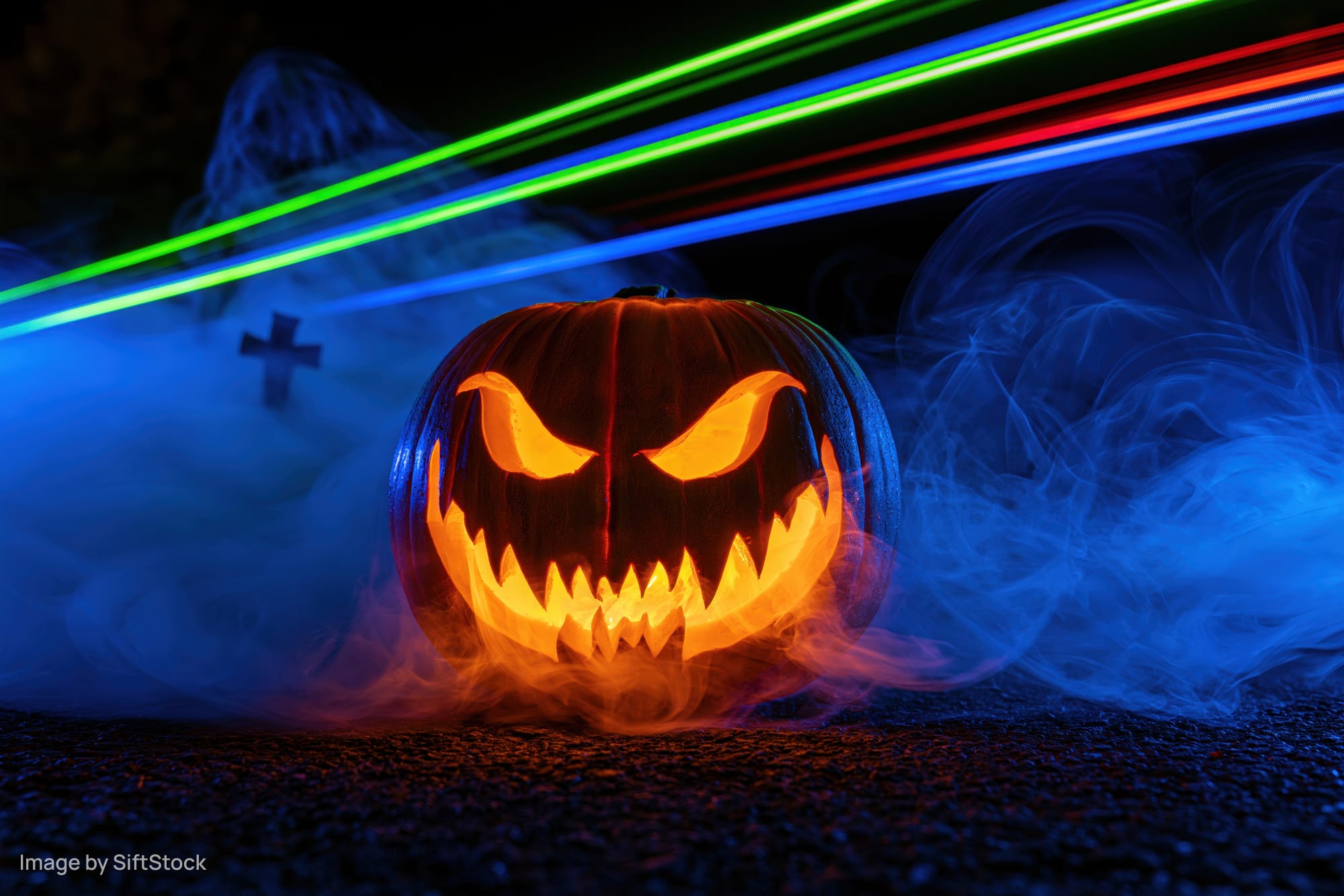 Carved jack-o-lantern with glowing evil grin surrounded by blue smoke and neon light trails at night
