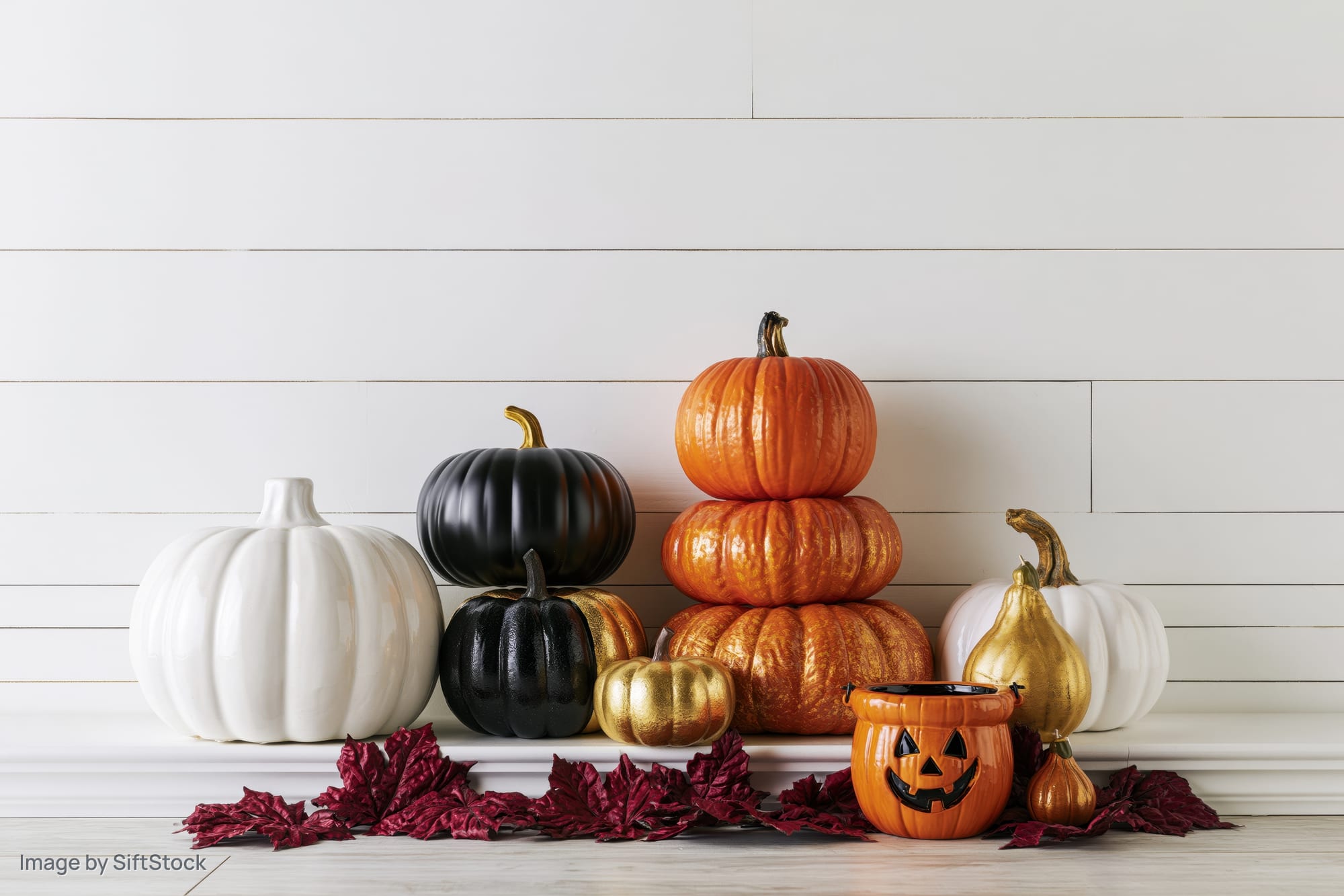 Decorative pumpkins and gourds arranged on a mantel with autumn leaves