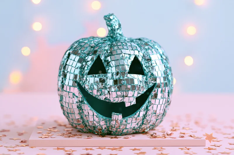 Teal disco mirror jack-o-lantern on pink surface with star confetti and bokeh lights
