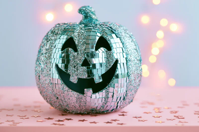 Teal glitter and mirror sequin jack-o-lantern on pink surface with star confetti and bokeh lights