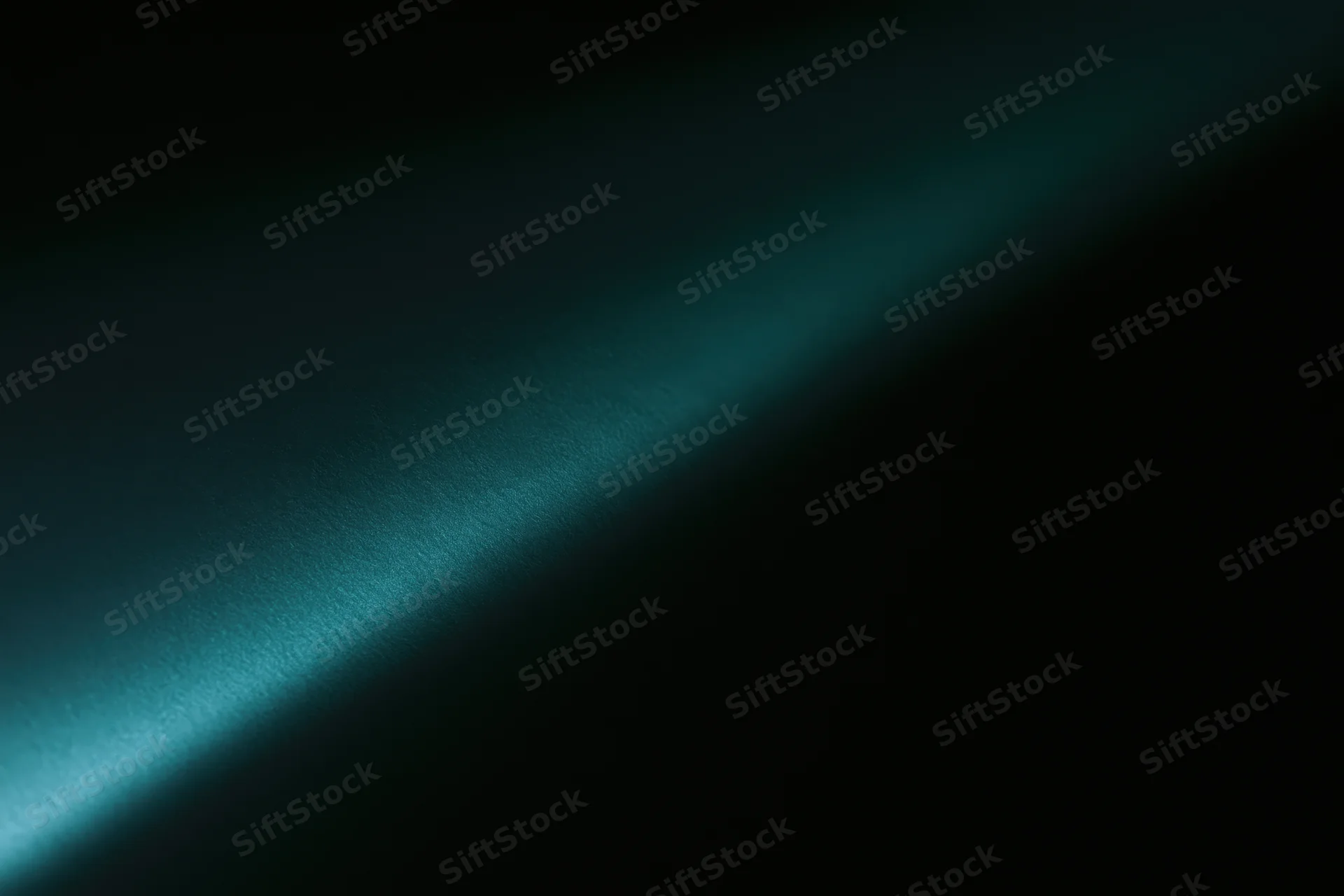 Diagonal band of soft teal-green light across dark surface