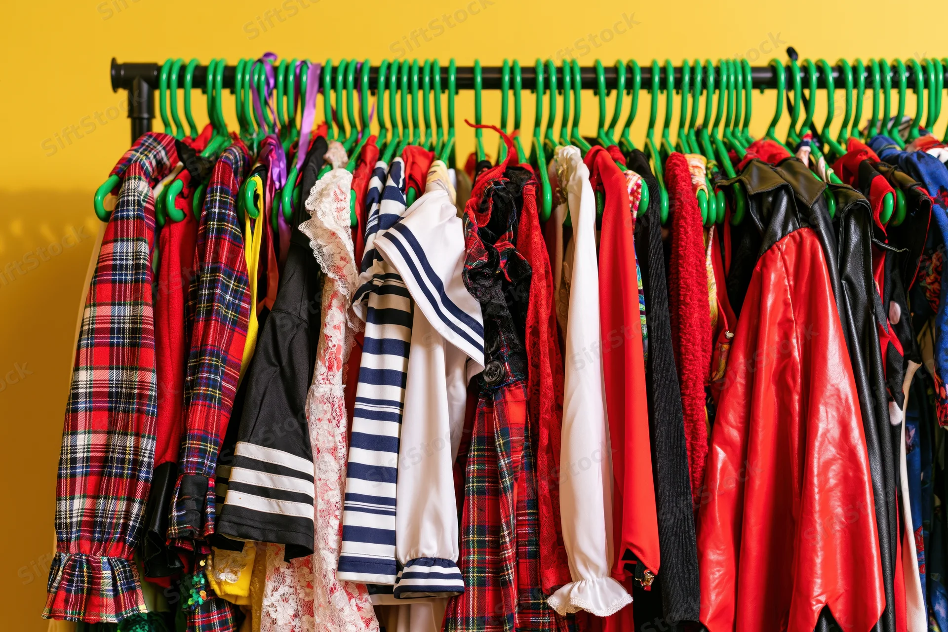 Colorful children's halloween costumes hanging on a green rack against a yellow wall