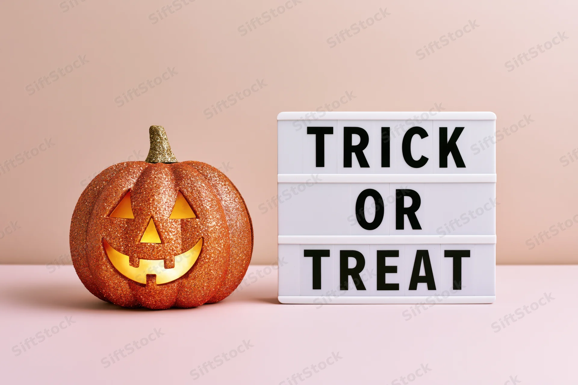 Glittery jack-o-lantern with glowing face next to trick or treat lightbox on pastel surface