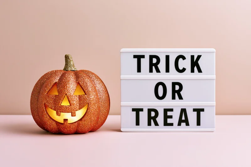 Glittery jack-o-lantern with glowing face next to trick or treat lightbox on pastel surface
