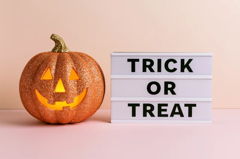 Glittery jack-o-lantern with carved face and glowing eyes beside a lightbox sign reading trick or treat on a pastel pink surface