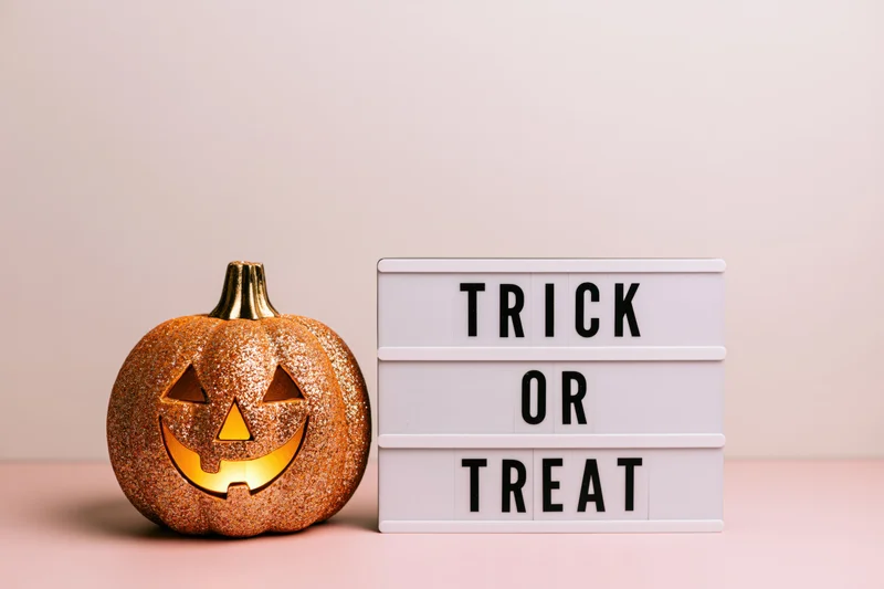Glittery gold jack-o-lantern with glowing face beside a white lightbox sign reading trick or treat on a pink surface