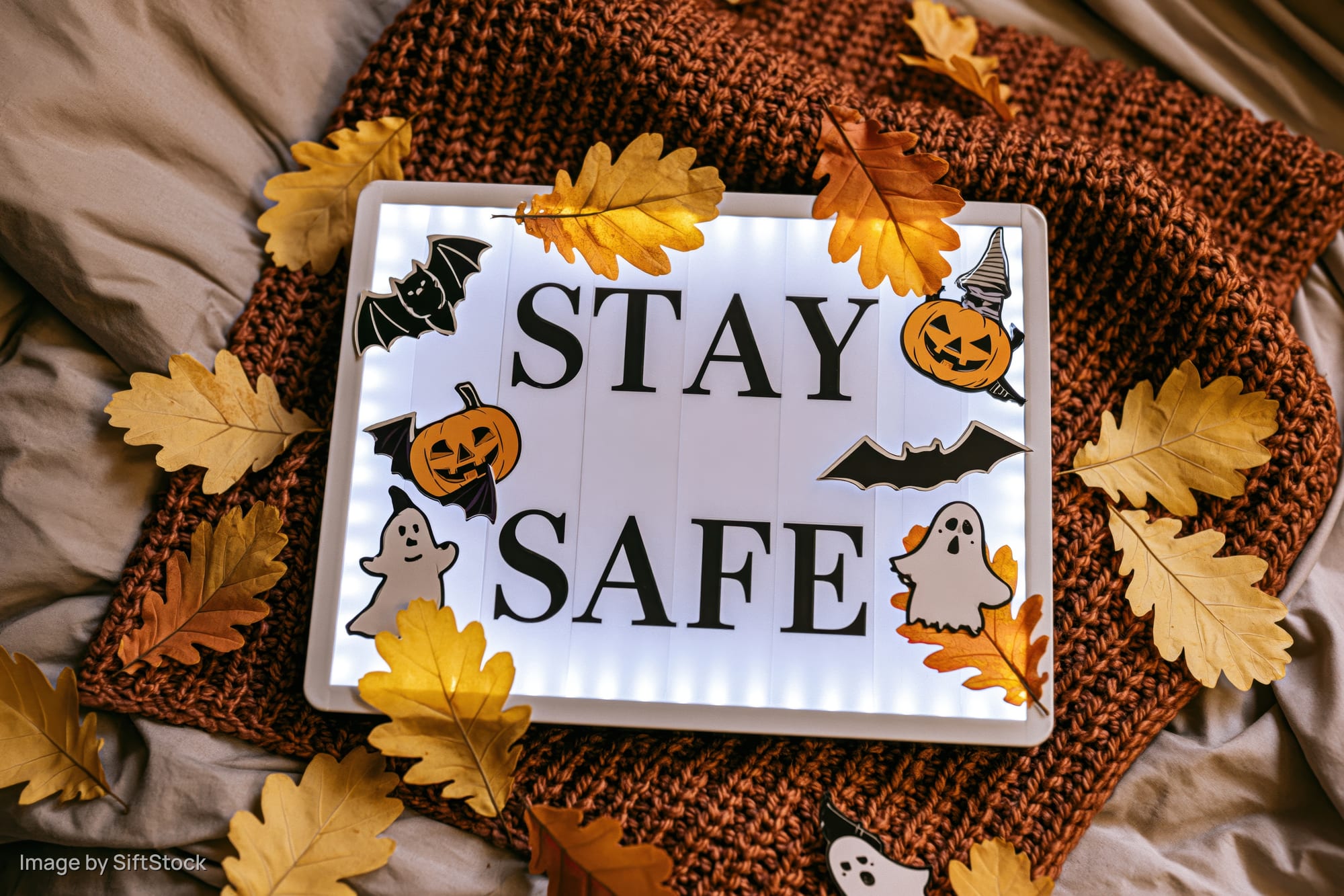 Glowing lightbox with stay safe message and halloween decorations on a knitted blanket