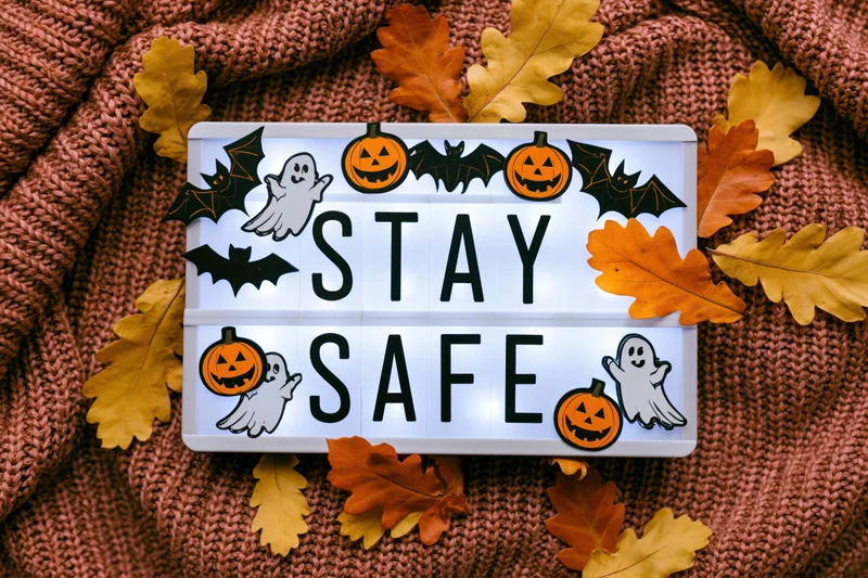 Glowing lightbox with stay safe message and halloween decorations on knitted sweater with autumn leaves