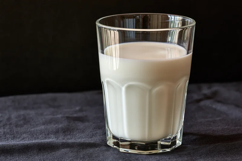 Half-full glass of milk on dark fabric surface