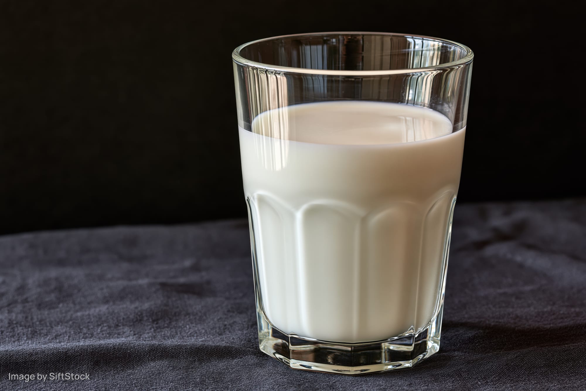 Half-full glass of milk on dark fabric surface