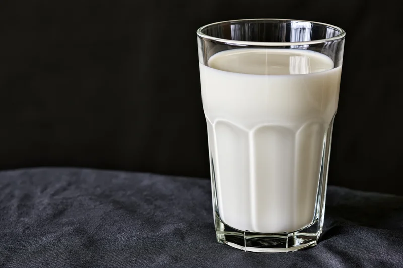 Glass tumbler filled with white milk on dark fabric surface