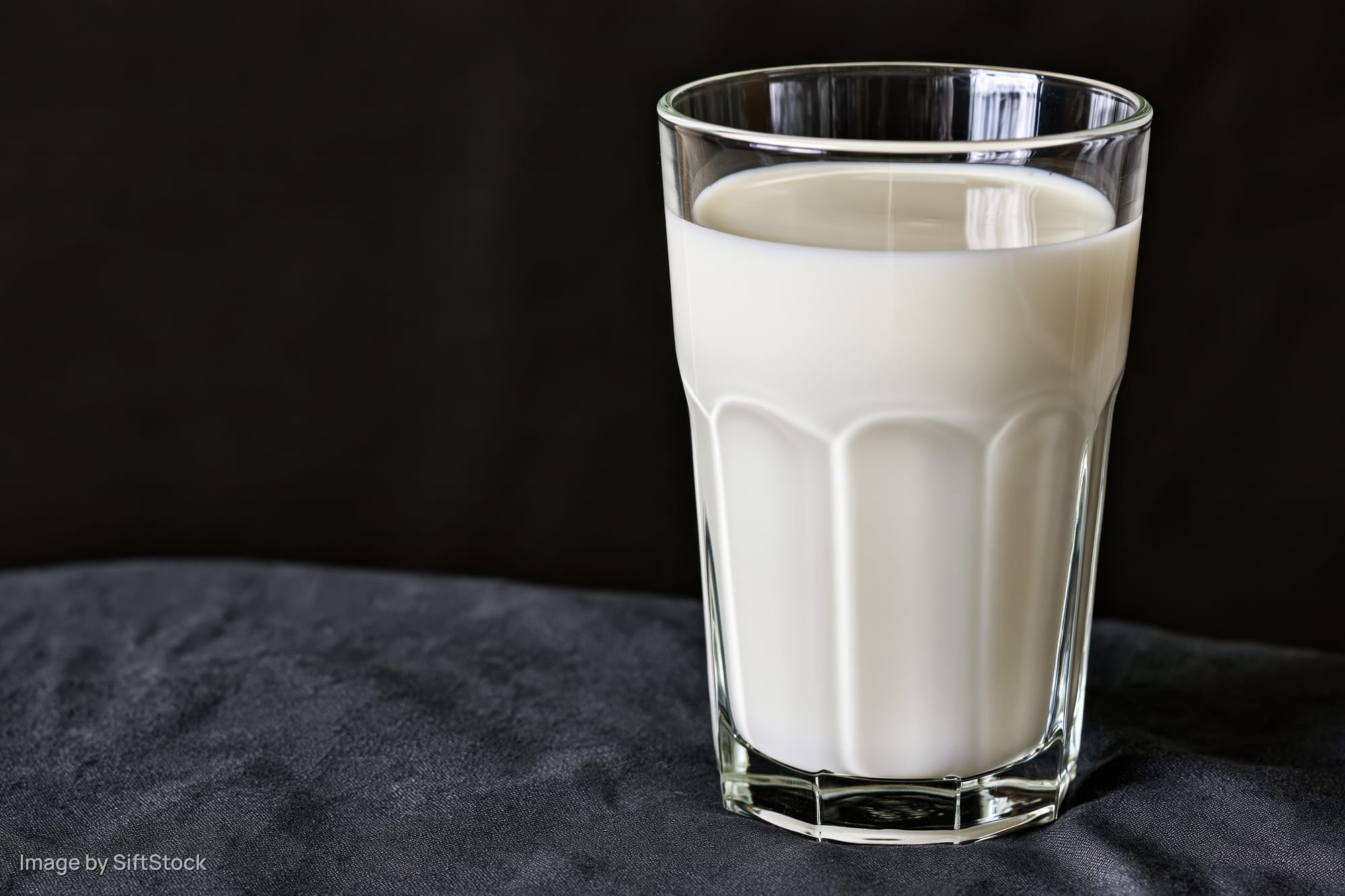 Glass tumbler filled with white milk on dark fabric surface