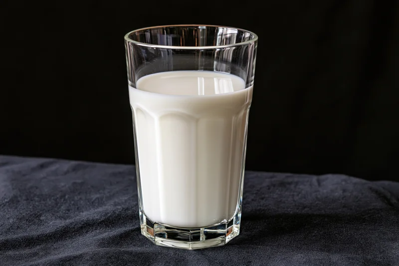 Glass tumbler filled with white milk on dark fabric surface