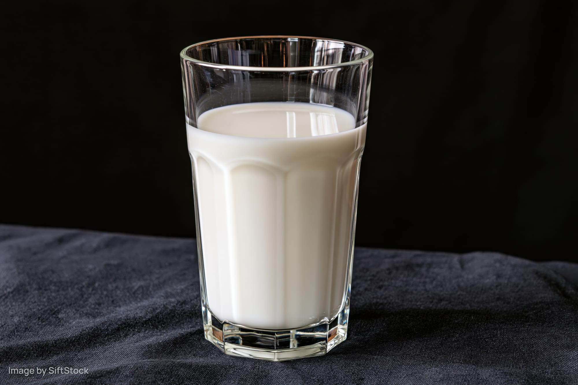 Glass tumbler filled with white milk on dark fabric surface