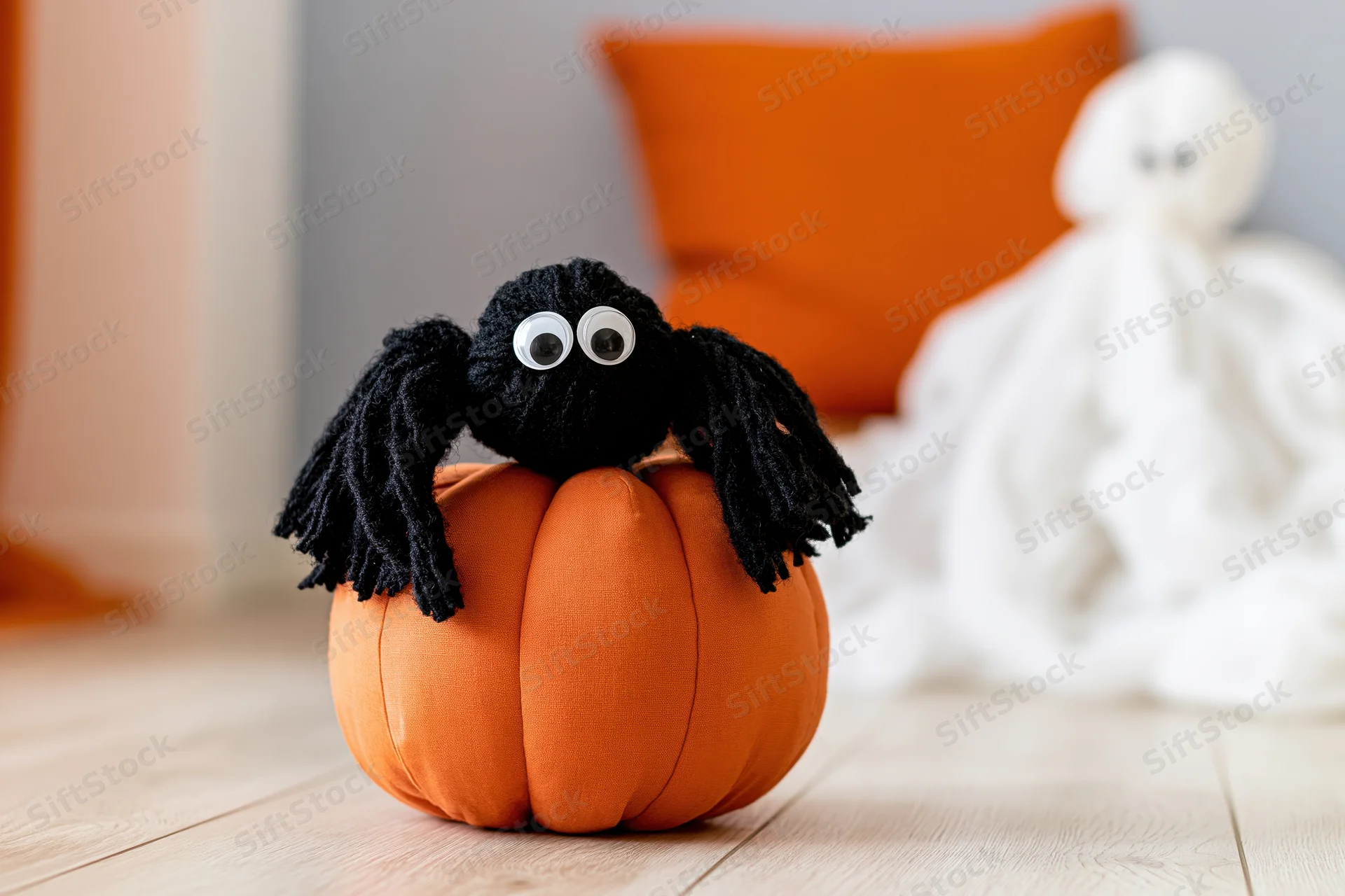 Handmade black yarn spider with googly eyes sitting on orange fabric pumpkin on wooden floor