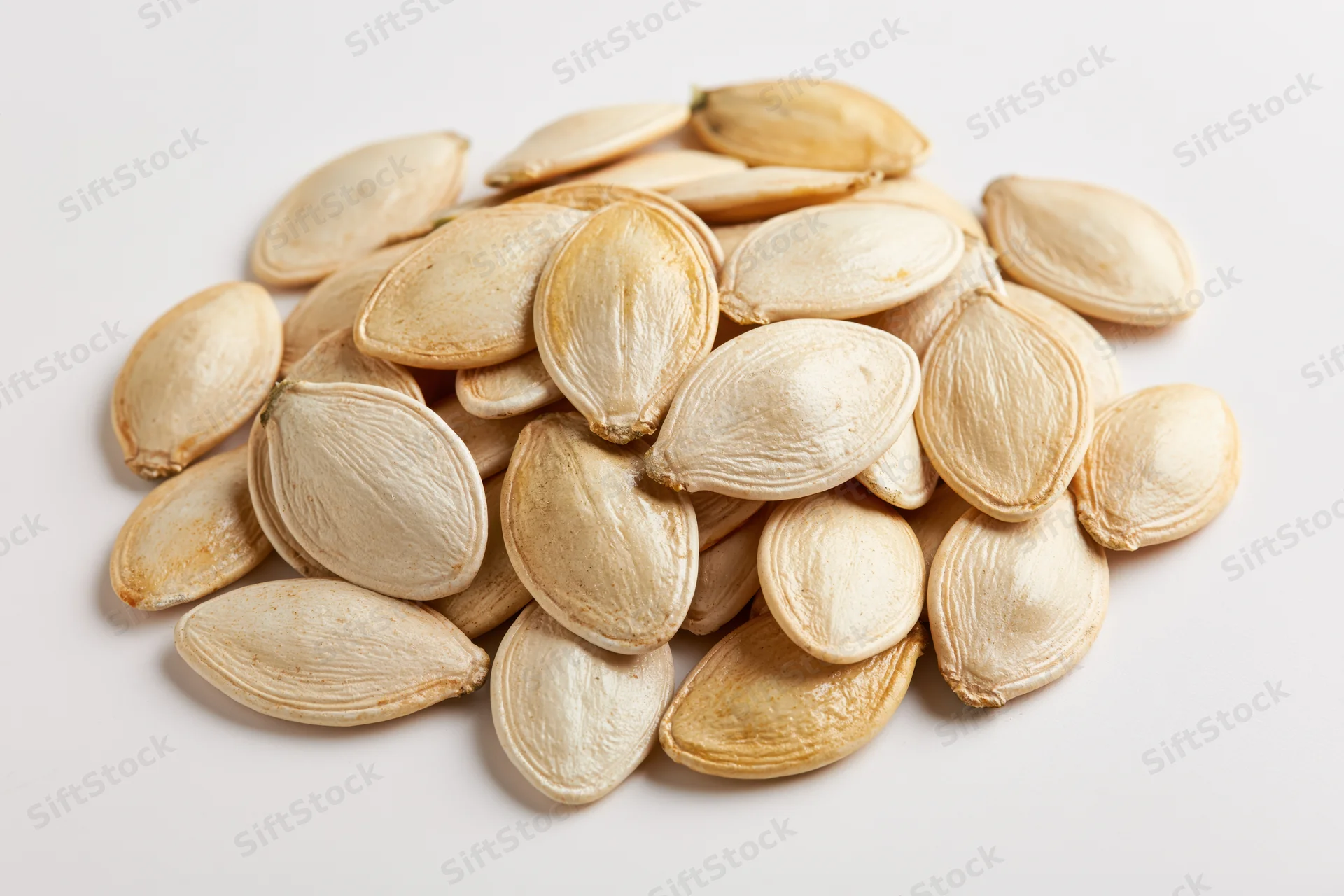 Pile of dried pumpkin seeds scattered on white surface