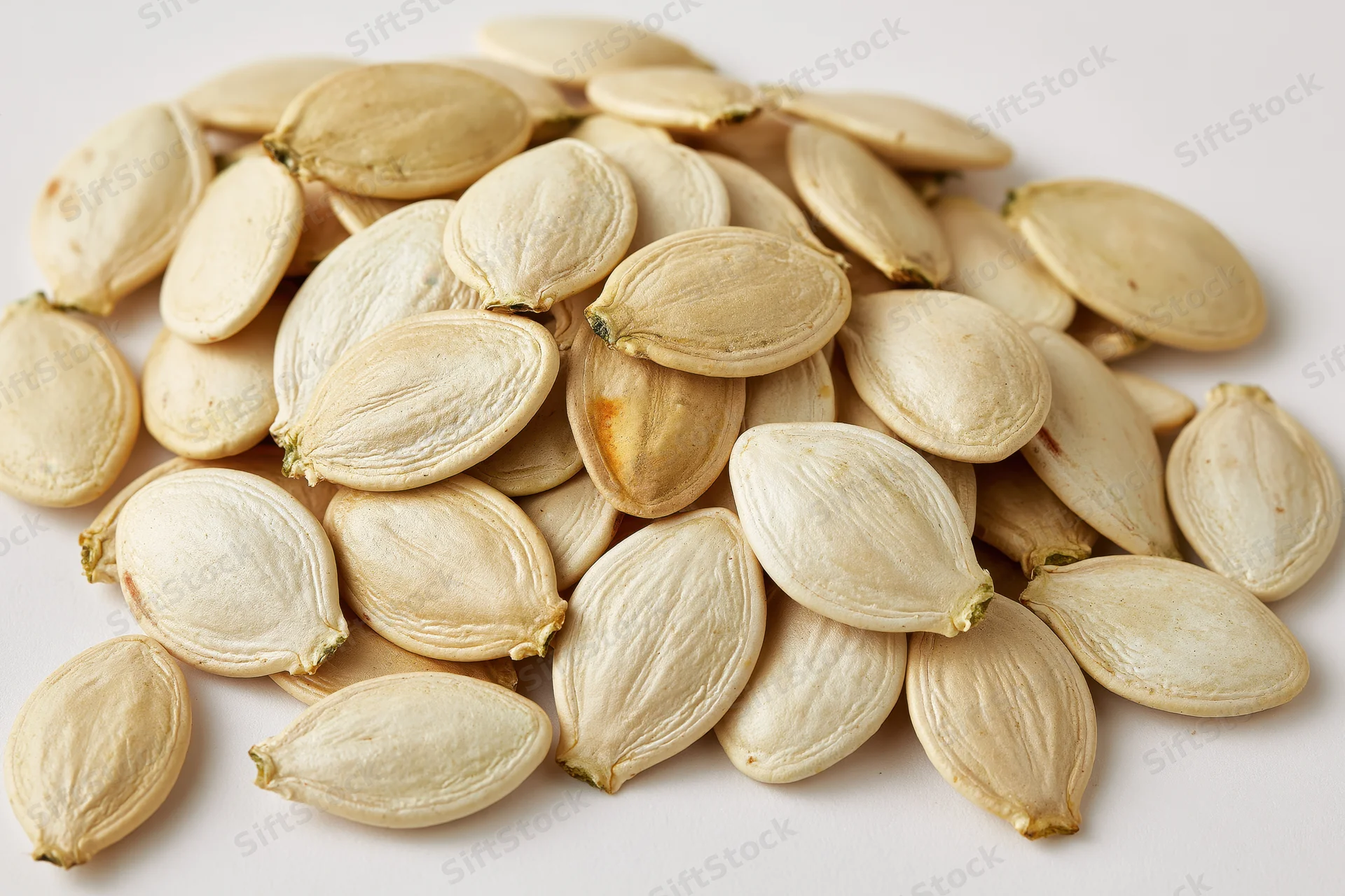 Dried pumpkin seeds scattered on a white surface