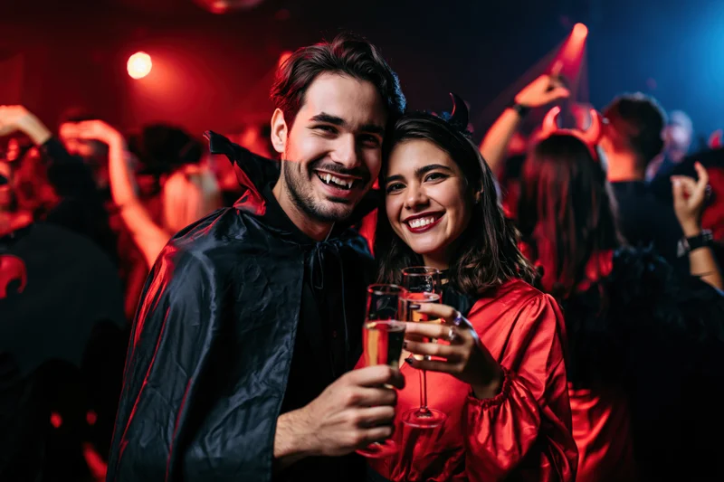 Couple in vampire and devil costumes toasting with champagne at a halloween party