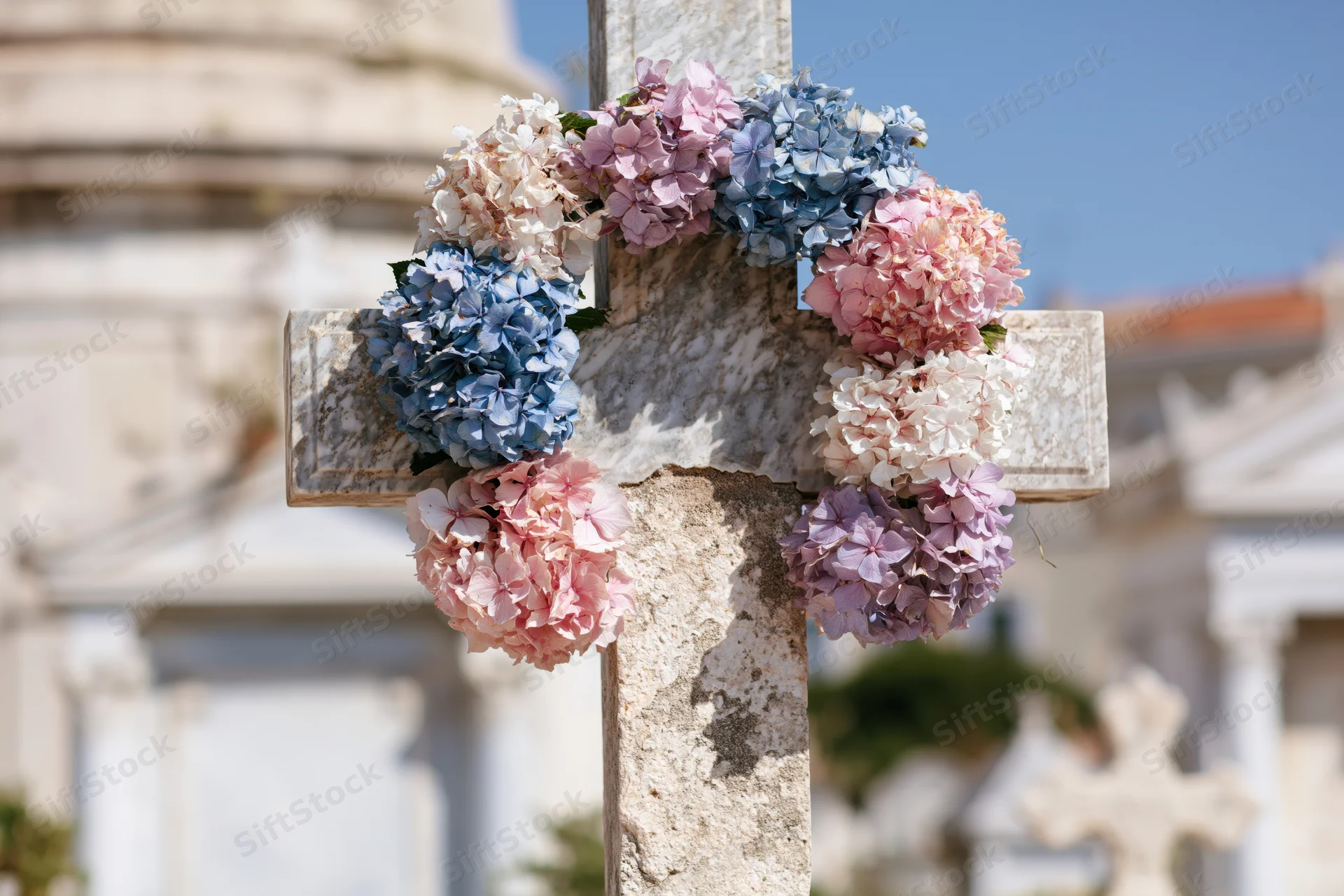 Marble cross in cemetery adorned with pink and blue hydrangea wreath