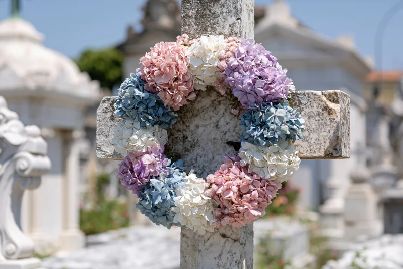 A marble cross in a cemetery adorned with a pastel hydrangea wreath