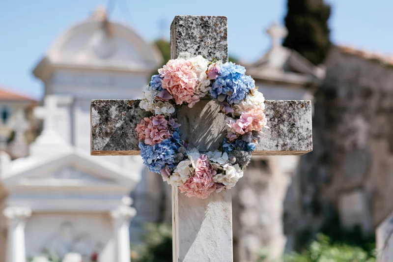 Stone cross in cemetery adorned with pink and blue hydrangea wreath