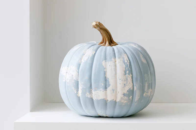 Painted blue pumpkin with distressed white paint on a white shelf