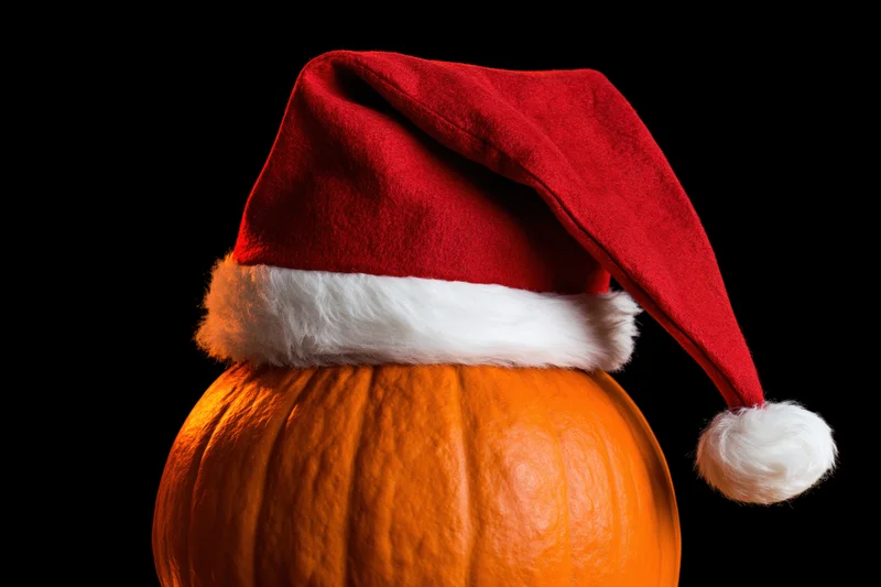 Pumpkin wearing a red santa hat against black background