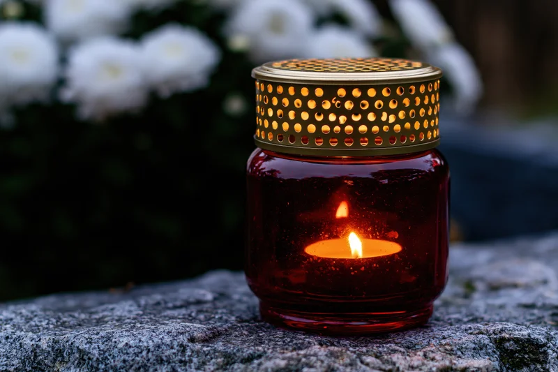 Red glass grave lantern with gold perforated lid lit on stone tombstone outdoors