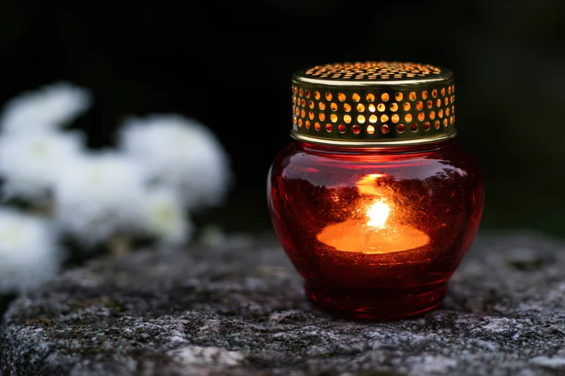 Red glass grave lantern with gold perforated lid lit on stone surface at night