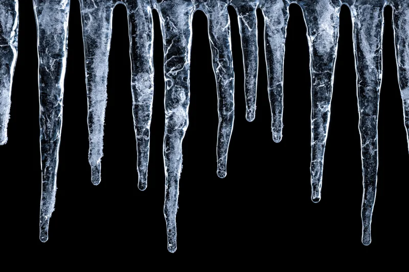 Row of natural icicles hanging down from the top edge against black background