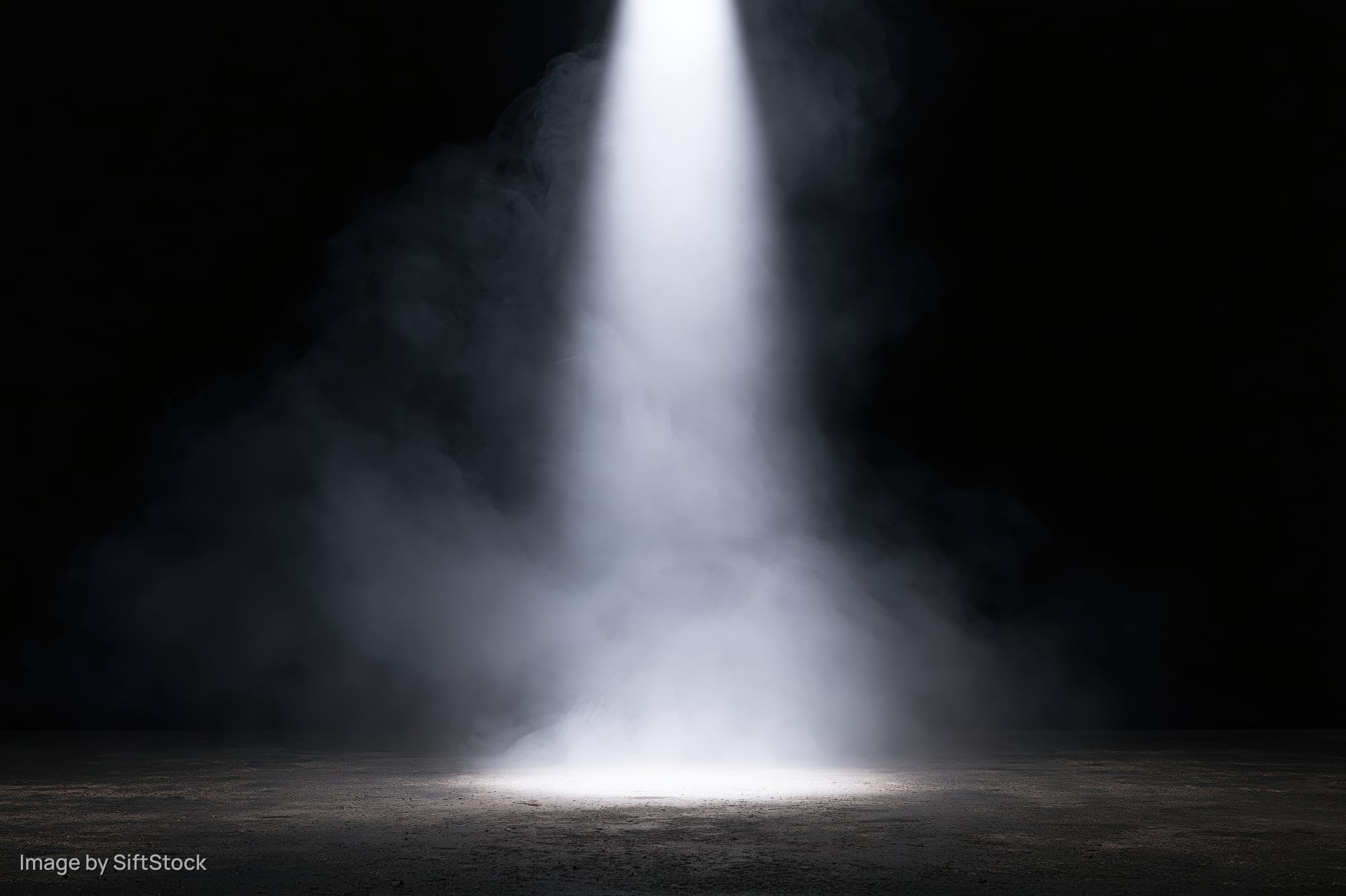A single spotlight beam cutting through smoke on a dark stage floor
