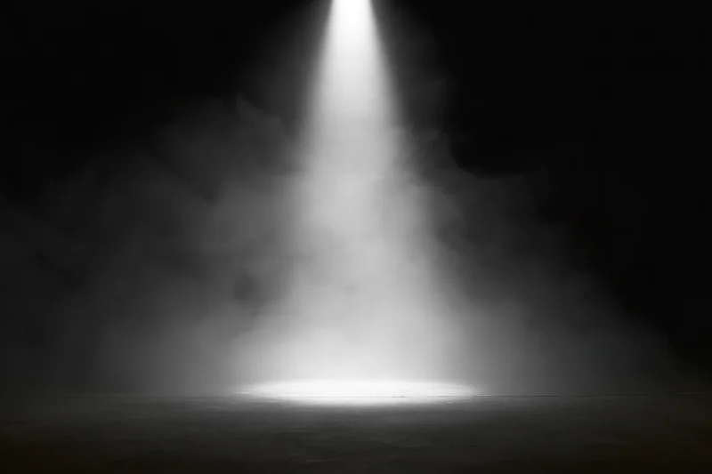 A single spotlight beam illuminating a smoky stage floor in darkness