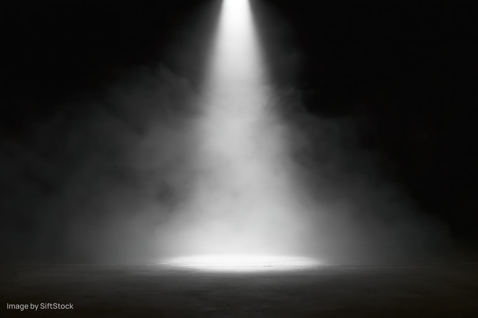A single spotlight beam illuminating a smoky stage floor in darkness