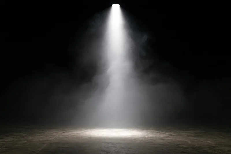 Single spotlight beam shining down through smoke onto empty concrete floor