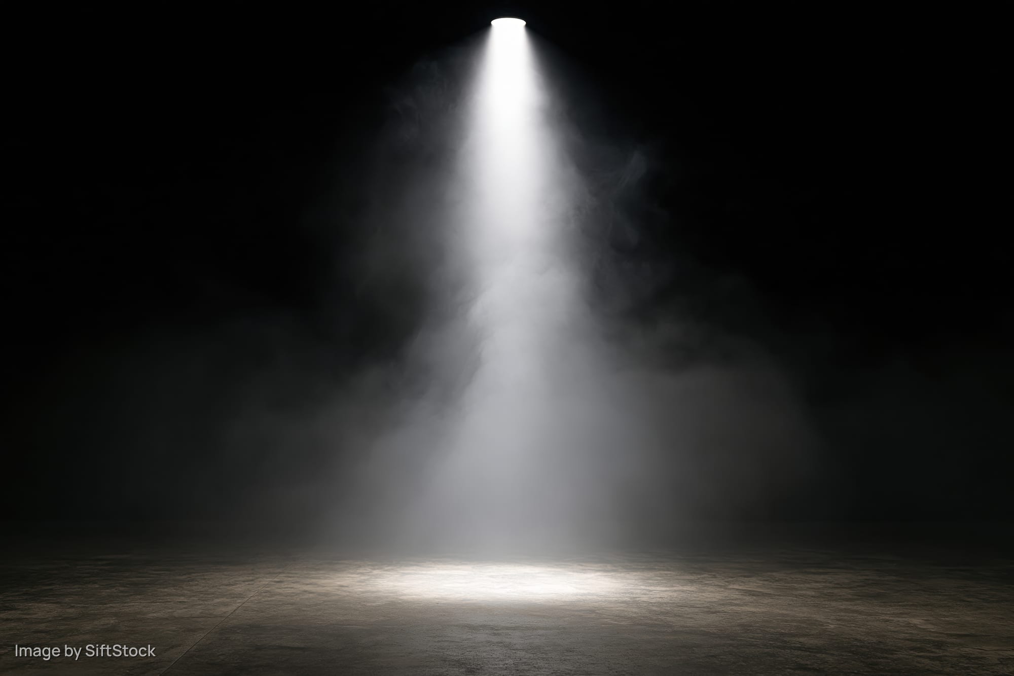 Single spotlight beam shining down through smoke onto empty concrete floor
