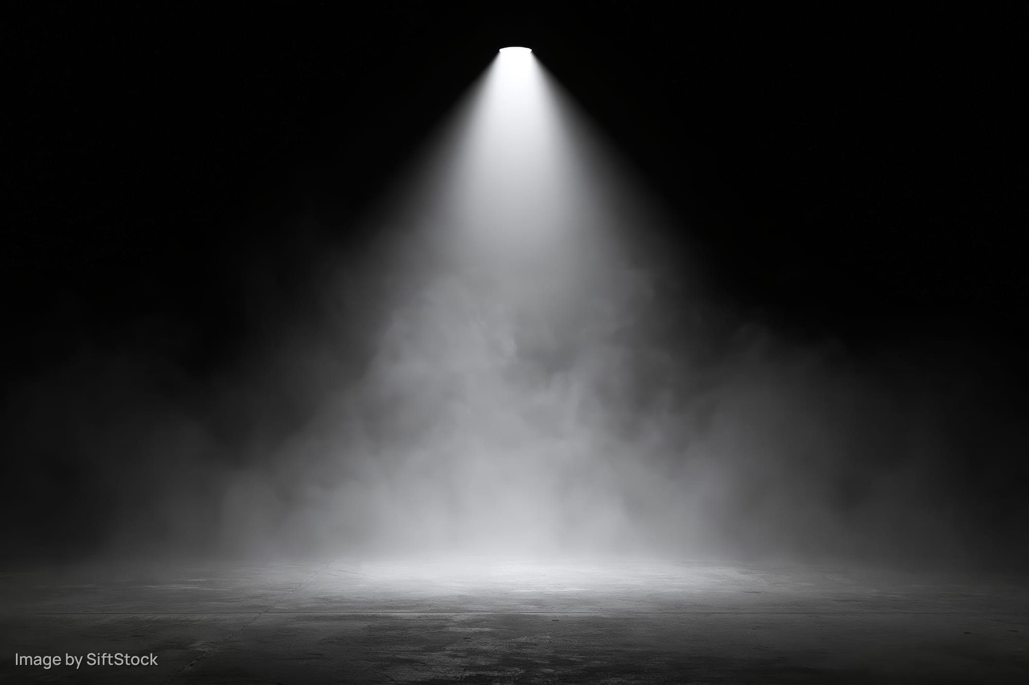 Spotlight beam cutting down through smoke onto empty stage floor