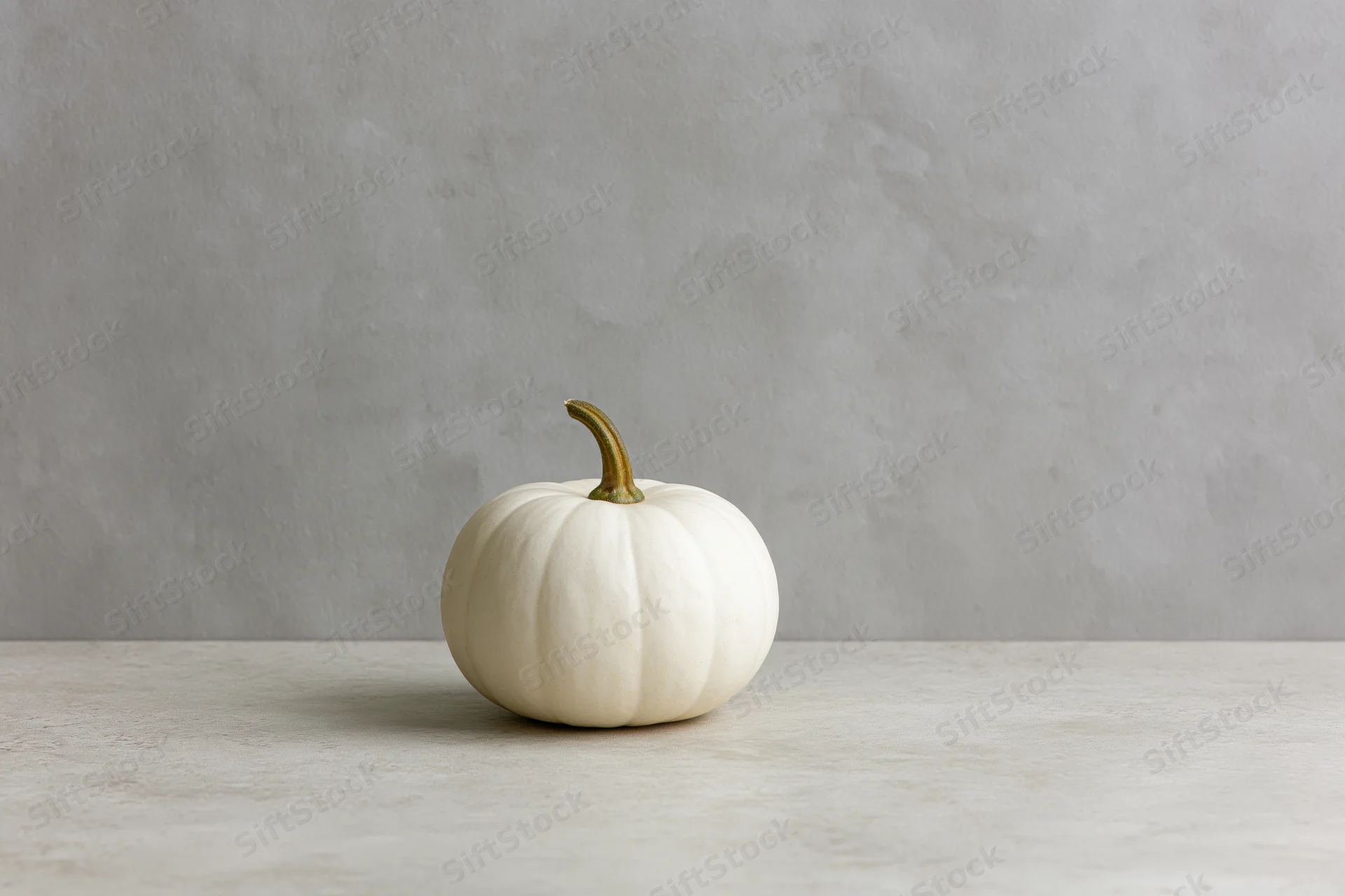 Small white pumpkin resting on a light gray surface against a concrete wall