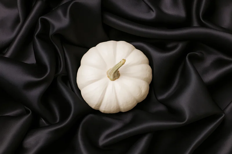 Small white pumpkin with pale green stem resting on black satin fabric