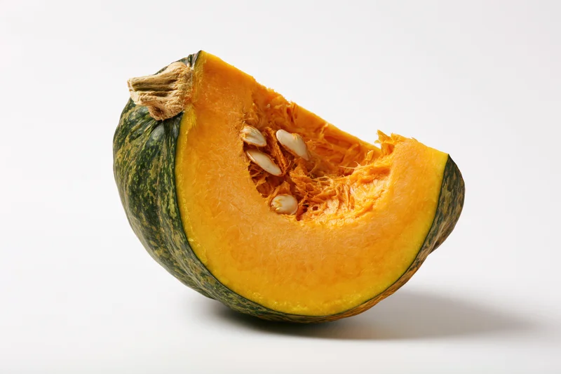 Wedge-shaped slice of kabocha squash cut open showing orange interior and seeds on white background