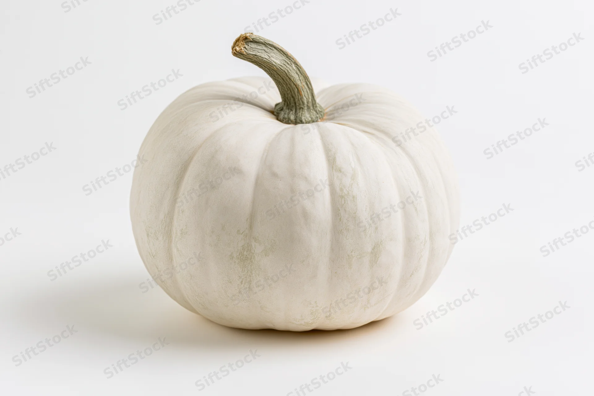 White heirloom pumpkin with ribbed texture and green stem on plain white surface