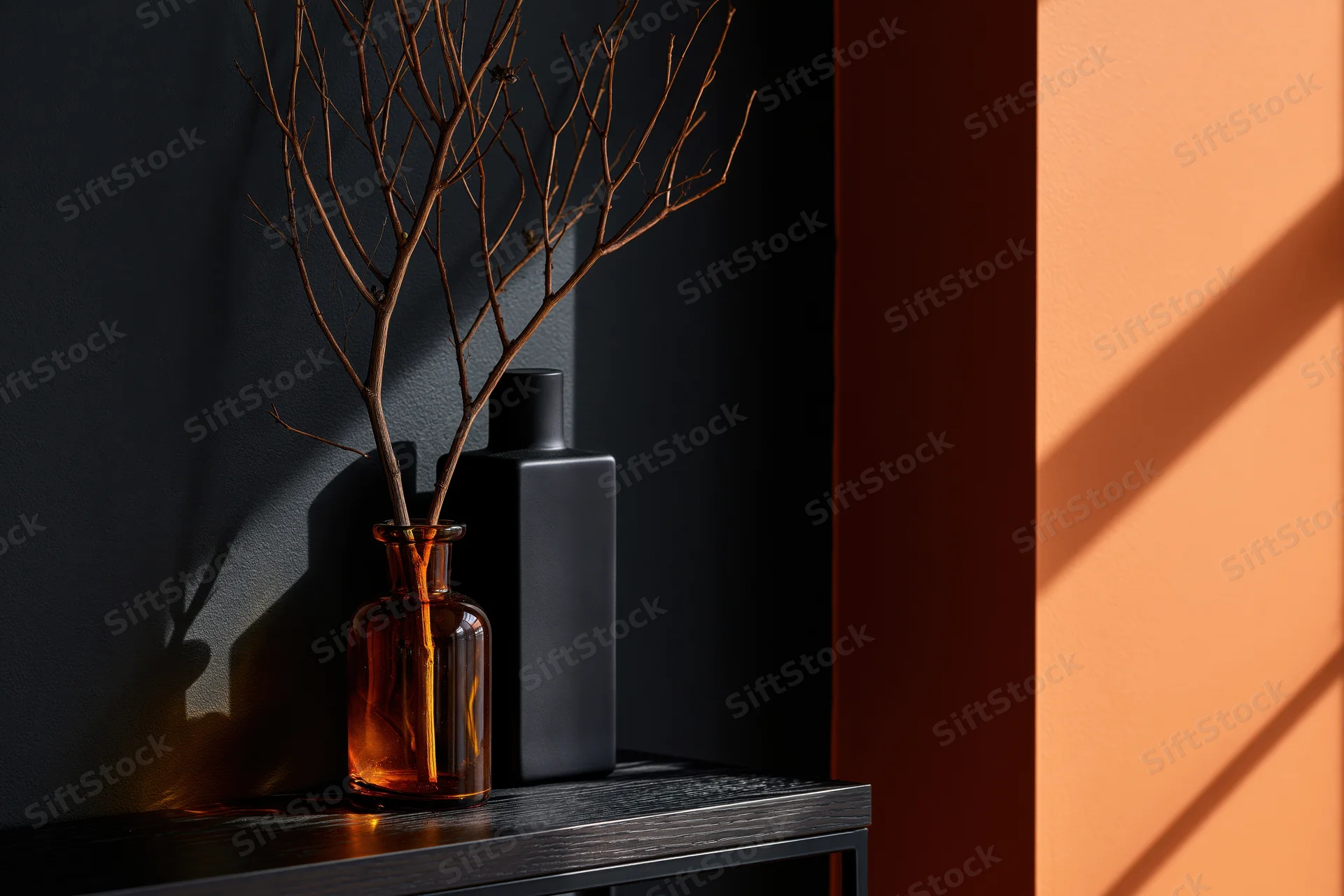 Amber glass vase with dried twig on dark shelf beside orange wall in sunlight