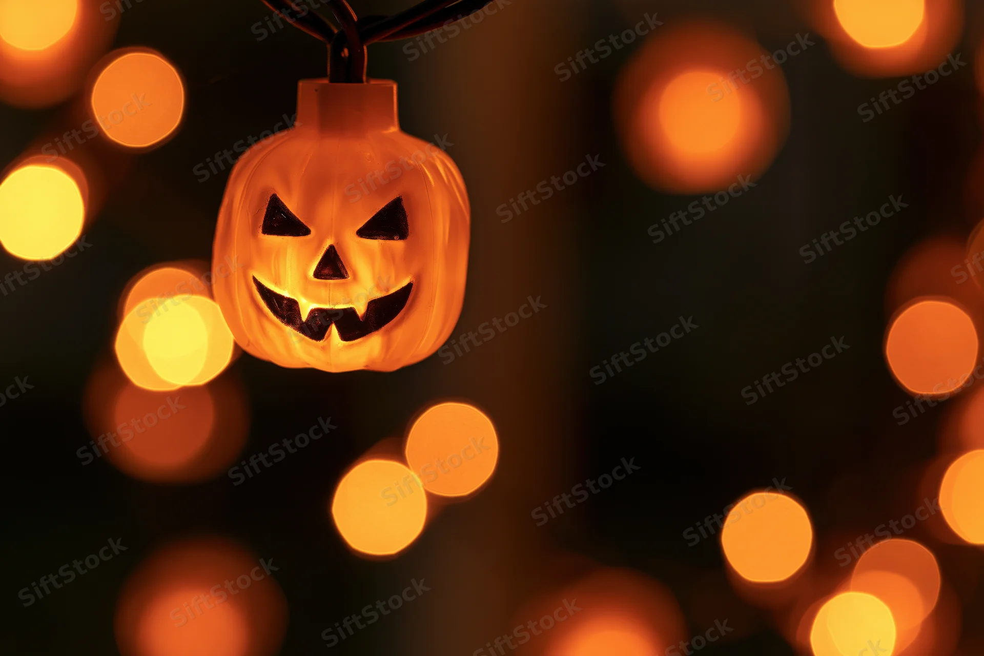 Glowing jack-o-lantern string light hanging in darkness with warm bokeh lights around