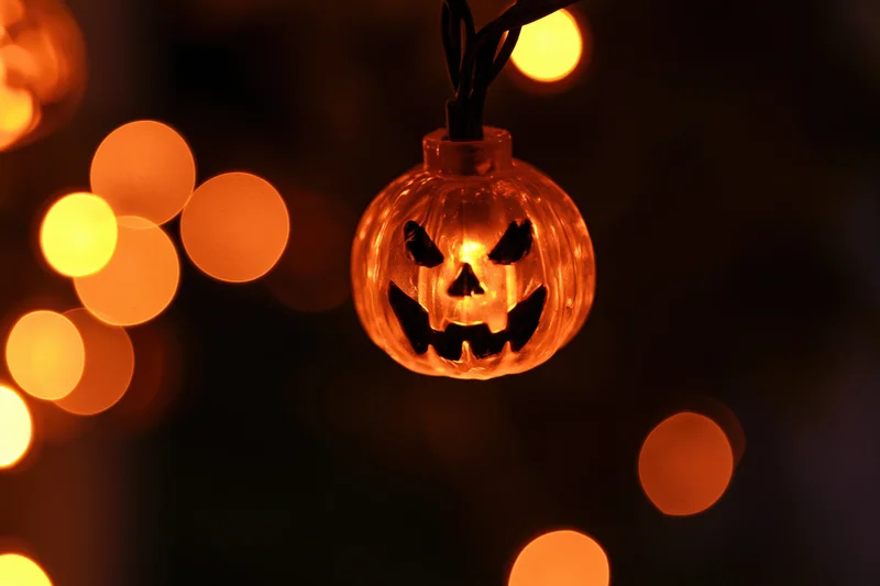 Glowing jack-o-lantern string light hanging in darkness with warm bokeh lights around