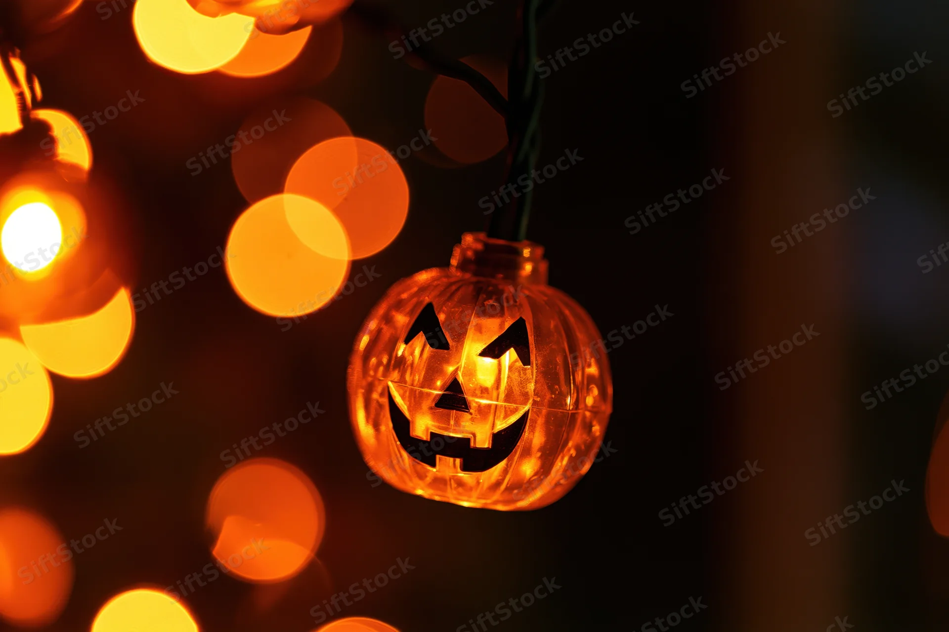 Glowing jack-o-lantern string light hanging in darkness with bokeh lights in background